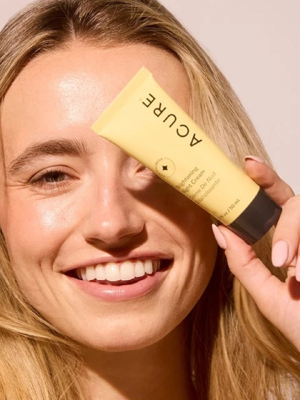 Model holding ACURE Brightening Night Cream beside her face