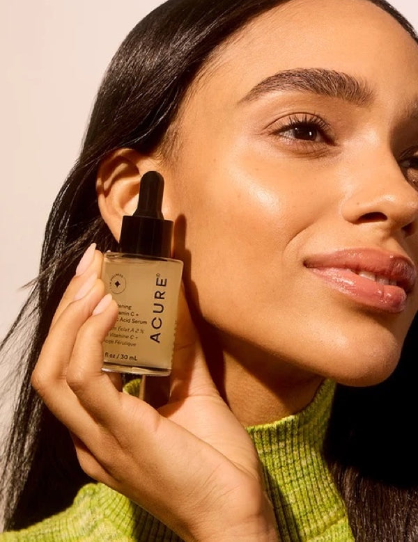 Model holding ACURE Brightening 2% Vitamin C & Ferulic Acid Serum beside her face