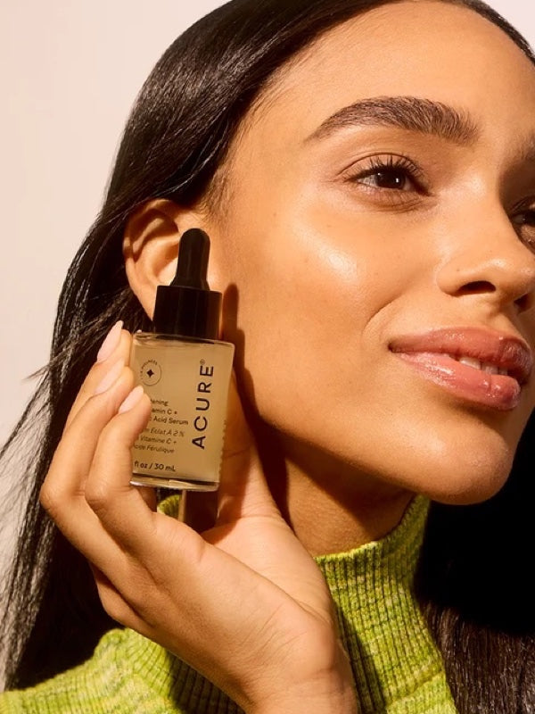 Model holding ACURE Brightening 2% Vitamin C & Ferulic Acid Serum beside her face