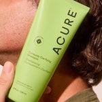 Model holding ACURE Curiously Clarifying Shampoo beside his face