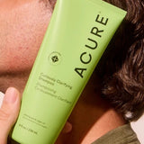 Model holding ACURE Curiously Clarifying Shampoo beside his face