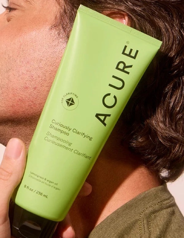 Model holding ACURE Curiously Clarifying Shampoo beside his face