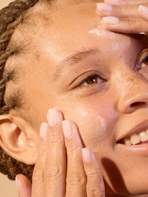 Model gently applying Acure Revived Radiance Overnight Mask to her face in warm sunlight.