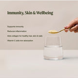 A hand holds a spoon of pale yellow Amazonia Vitamin C powder above a glass of water. The graphic lists claims for immune support, reduced inflammation, collagen for hair, skin and nails, and iron absorption.