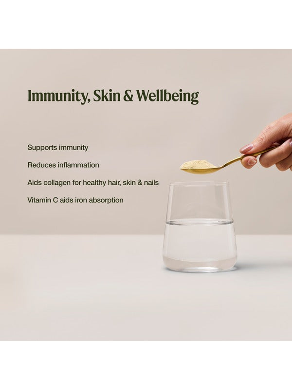 A hand holds a spoon of pale yellow Amazonia Vitamin C powder above a glass of water. The graphic lists claims for immune support, reduced inflammation, collagen for hair, skin and nails, and iron absorption.