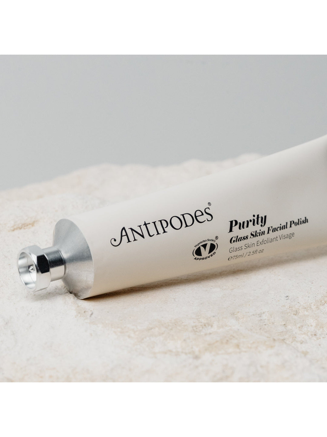 Antipodes Purity Glass Skin Facial Polish tube lying diagonally on a cream towel, with black lettering along its pale silver body and a silver cap at the left.