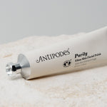Antipodes Purity Glass Skin Facial Polish tube lying diagonally on a cream towel, with black lettering along its pale silver body and a silver cap at the left.