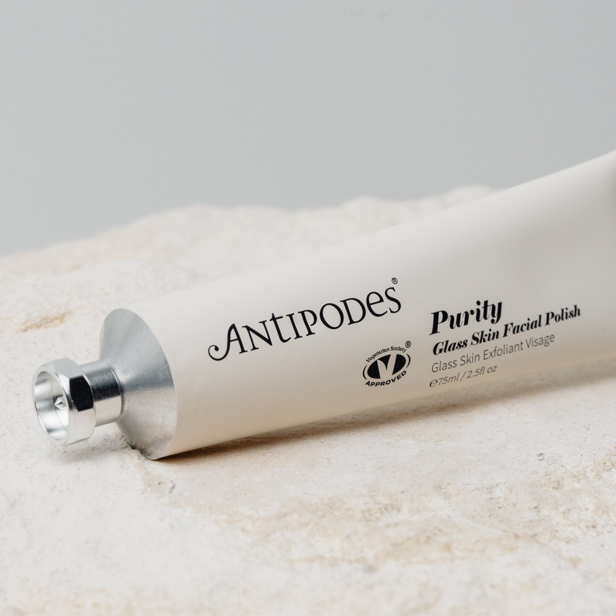 Antipodes Purity Glass Skin Facial Polish tube lying diagonally on a cream towel, with black lettering along its pale silver body and a silver cap at the left.