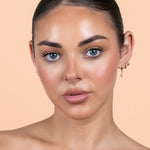 Avocado Zinc SPF 50 Physical Bronzing Drops shown on a model's face, with a warm bronzed finish across her cheeks and forehead against a peach background.
