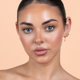 Avocado Zinc SPF 50 Physical Bronzing Drops shown on a model's face, with a warm bronzed finish across her cheeks and forehead against a peach background.