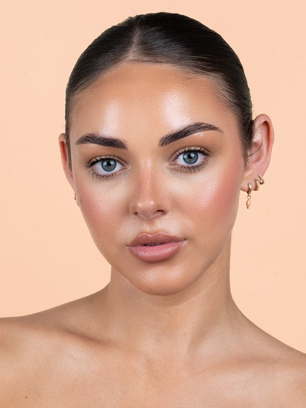 Avocado Zinc SPF 50 Physical Bronzing Drops shown on a model's face, with a warm bronzed finish across her cheeks and forehead against a peach background.