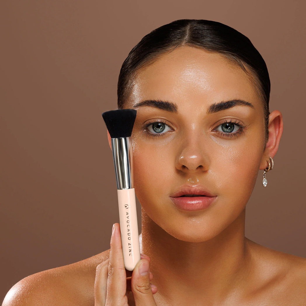 Model holding the Avocado Zinc SPF Kabuki Brush beside her face
