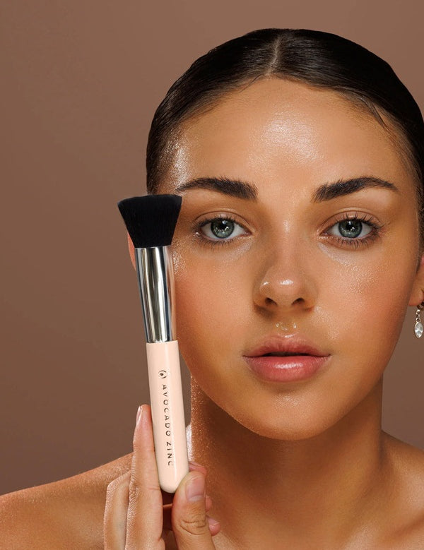 Model holding the Avocado Zinc SPF Kabuki Brush upright against her cheek.