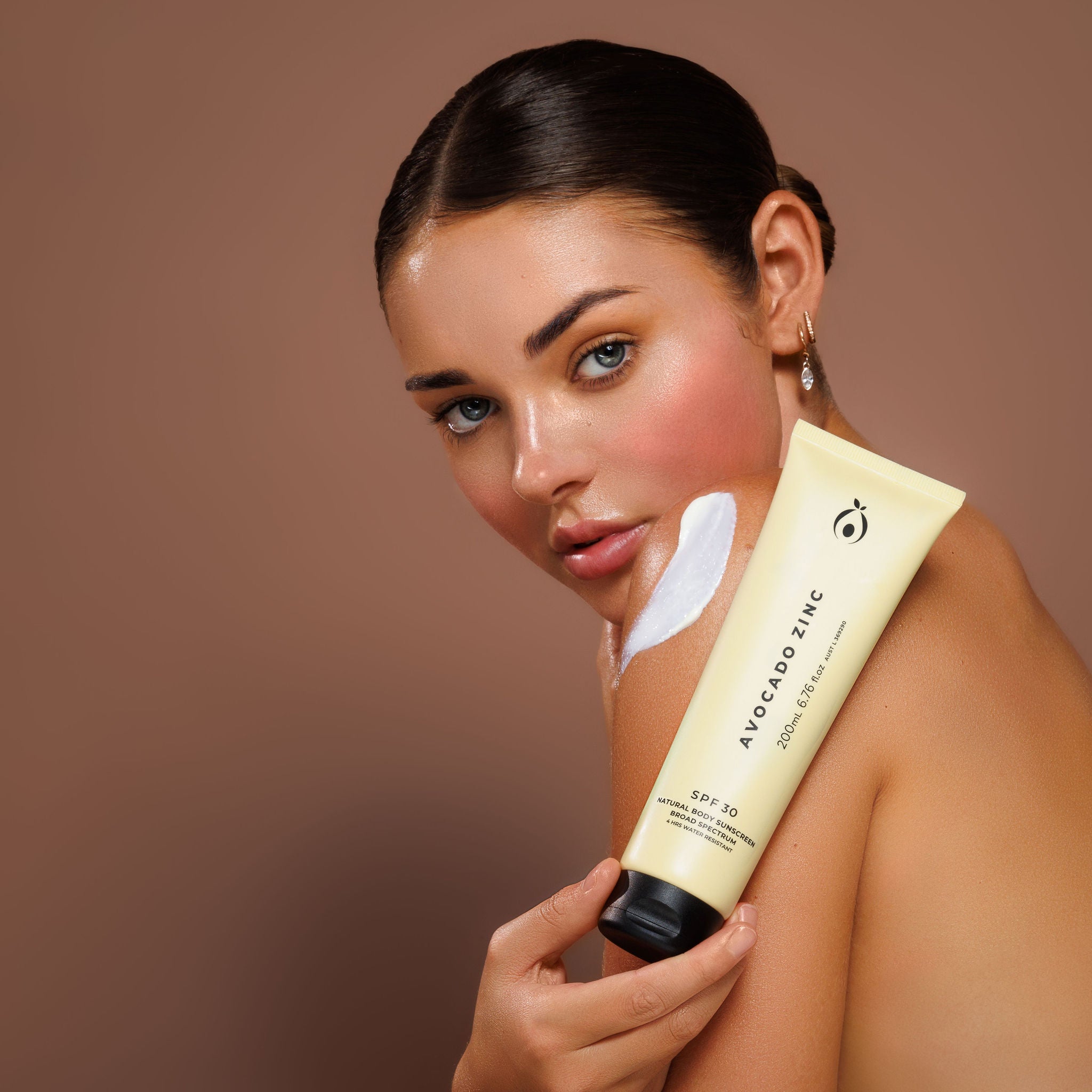 Model holding Avocado Zinc SPF 30 Natural Body Sunscreen with sunscreen applied to her shoulder