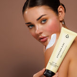 Model holding Avocado Zinc SPF30 Natural Body Sunscreen with a visible swipe of cream on her shoulder.