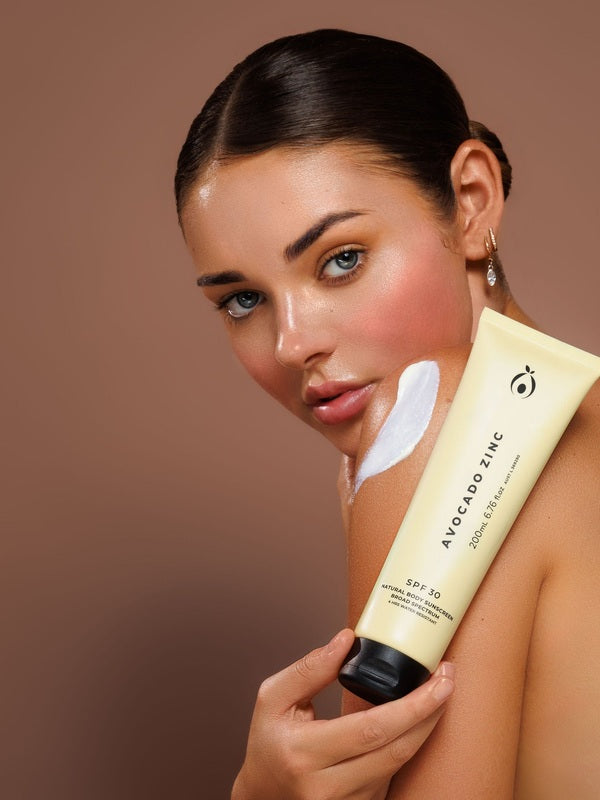 Model holding Avocado Zinc SPF30 Natural Body Sunscreen with a visible swipe of cream on her shoulder.