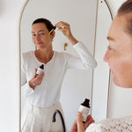 Woman applying Mukti Vital A Vitamin Booster in front of an arched mirror