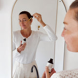 Woman applying Mukti Vital A Vitamin Booster in front of an arched mirror