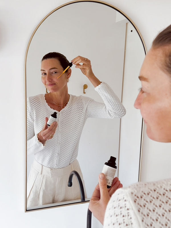Woman applying Mukti Vital A Vitamin Booster in front of an arched mirror