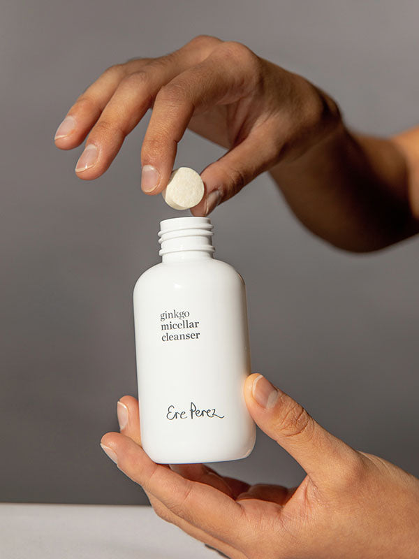 Hands dropping an Ere Perez Ginkgo Micellar Cleanser tablet into the refillable white bottle