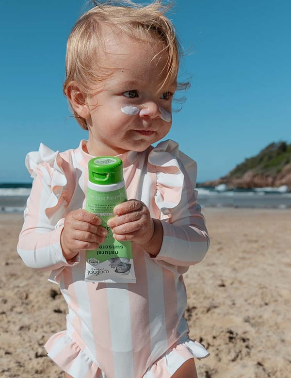 Baby holding Wotnot Natural Baby Sunscreen SPF 30 at the beach