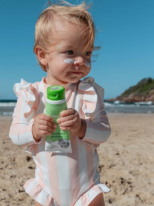 Baby holding Wotnot Natural Baby Sunscreen SPF 30 at the beach