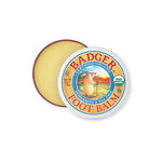 A round tin of Badger Foot Balm 56g, certified organic with peppermint and tea tree scent, partially open to show the balm. The lid displays a badger illustration and the USDA Organic label.