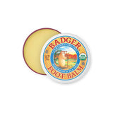 A round tin of Badger Foot Balm 56g, certified organic with peppermint and tea tree scent, partially open to show the balm. The lid displays a badger illustration and the USDA Organic label.