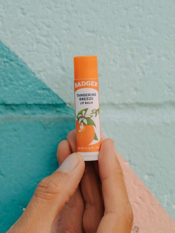 Badger Tangerine Breeze Lip Balm held against a colourful wall