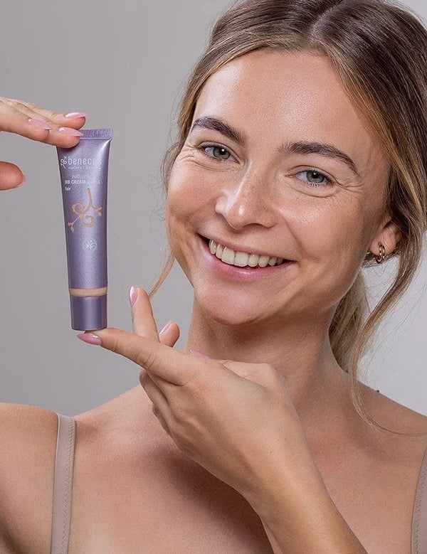 Smiling model holding a tube of Benecos BB Cream beside her face.