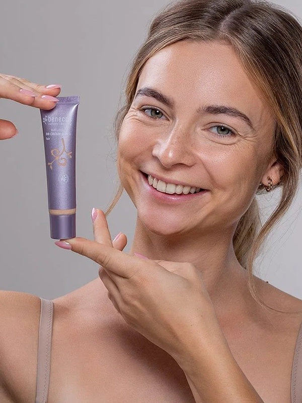 Smiling model holding a tube of Benecos BB Cream beside her face.
