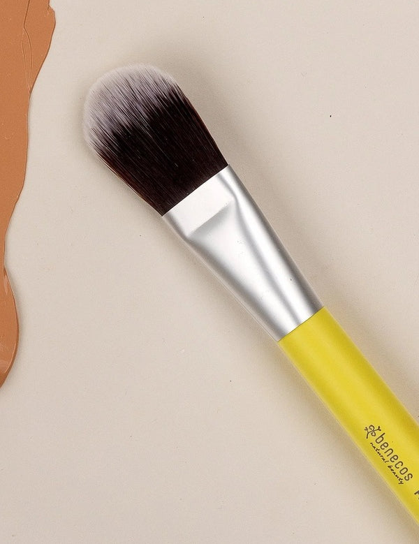 Benecos Foundation Brush with yellow handle arranged diagonally on a neutral cream background with terracotta shapes.
