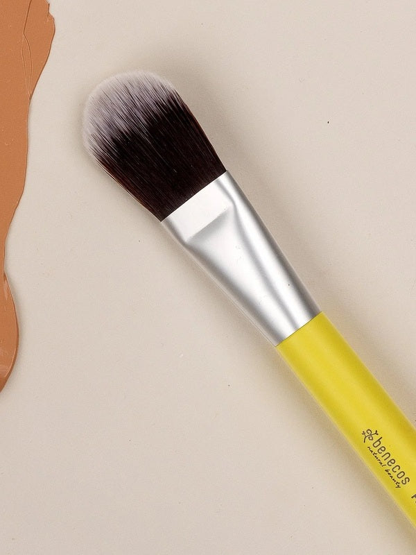 Benecos Foundation Brush with yellow handle arranged diagonally on a neutral cream background with terracotta shapes.