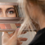 Model viewing her eye in the mirror of an open Benecos Large Beauty ID Palette with refill pans below.