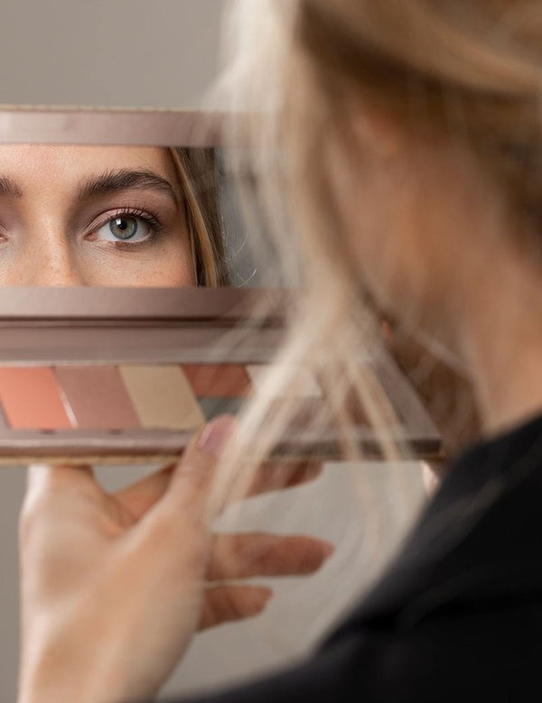 Model viewing her eye in the mirror of an open Benecos Large Beauty ID Palette with refill pans below.