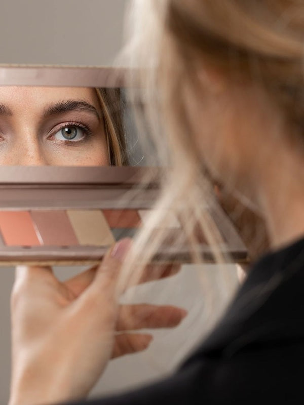 Model viewing her eye in the mirror of an open Benecos Large Beauty ID Palette with refill pans below.