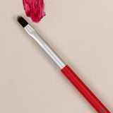 Red-handled Benecos Lip Brush arranged beside a vivid crimson lipstick swatch.
