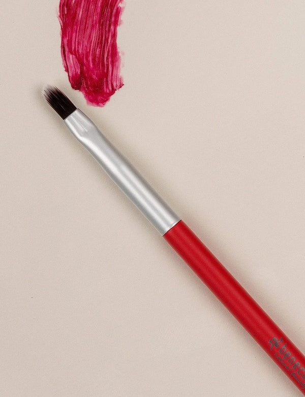 Red-handled Benecos Lip Brush arranged beside a vivid crimson lipstick swatch.