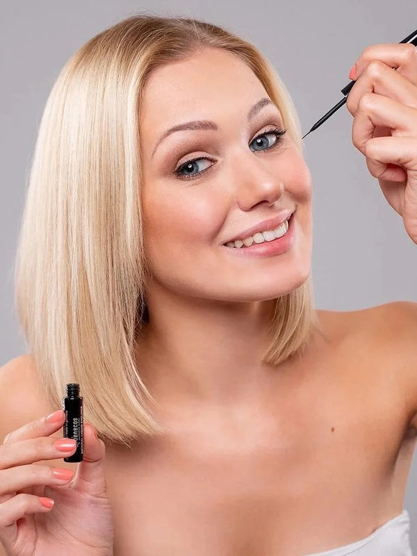 Model applying Benecos Liquid Eyeliner in Deep Black while holding the open liner bottle.