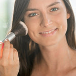 Model applying Benecos Natural Mineral Powder to her cheek with a large face brush.