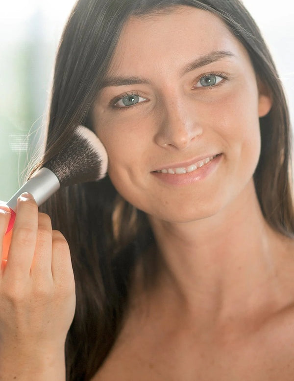 Model applying Benecos Natural Mineral Powder to her cheek with a large face brush.