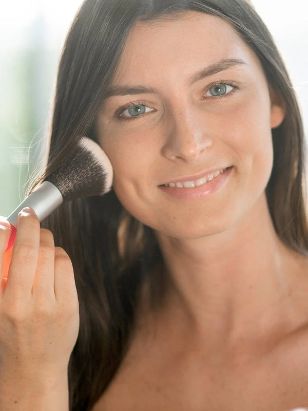 Model applying Benecos Natural Mineral Powder to her cheek with a large face brush.