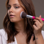 Model applying Benecos Mission Invisible Mattifying Translucent Powder to her cheek with a pink-handled brush.