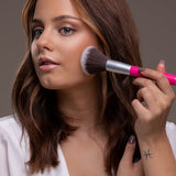 Model applying Benecos Mission Invisible Mattifying Translucent Powder to her cheek with a pink-handled brush.