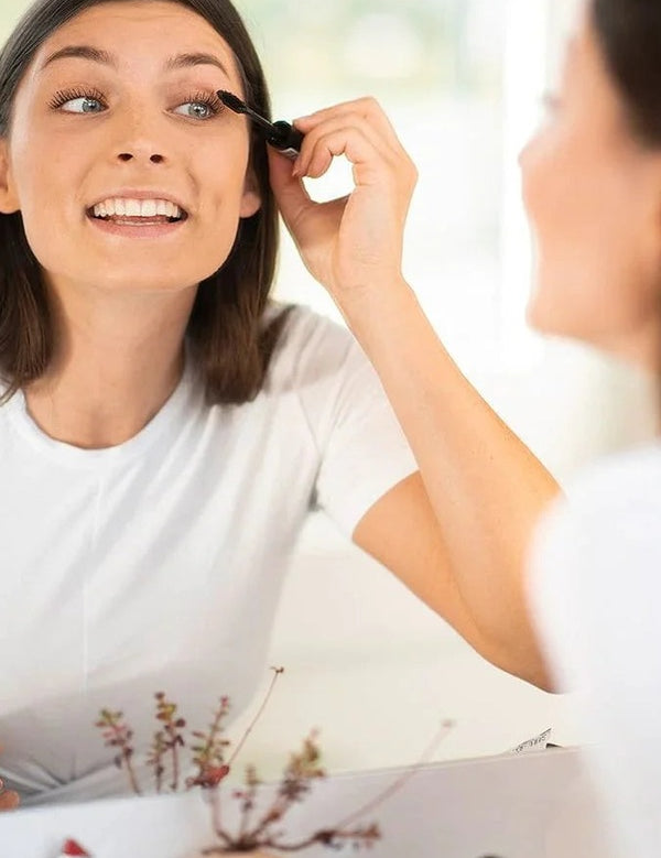 Model applying Benecos Vegan Volume Mascara in Black Magic while looking into a mirror.