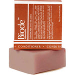Dusty pink rectangular Biode Into the Earth conditioner bar beneath a terracotta carton printed with white lines and lettering.