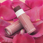 Two Biode Lip & Cheek Tinted Balm tubes in Lilly Pilly arranged on vivid pink flower petals.