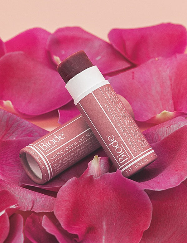 Two Biode Lip & Cheek Tinted Balm tubes in Lilly Pilly arranged on vivid pink flower petals.