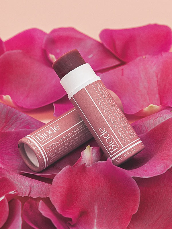 Two Biode Lip & Cheek Tinted Balm tubes in Lilly Pilly arranged on vivid pink flower petals.