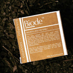 Biode Into The Sunset Shampoo Bar packaging resting on a dark natural ground, showing the back label and product details.